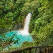 Travelers descend wooden stairs through the rainforest in Central America, heading towards a cascading waterfall