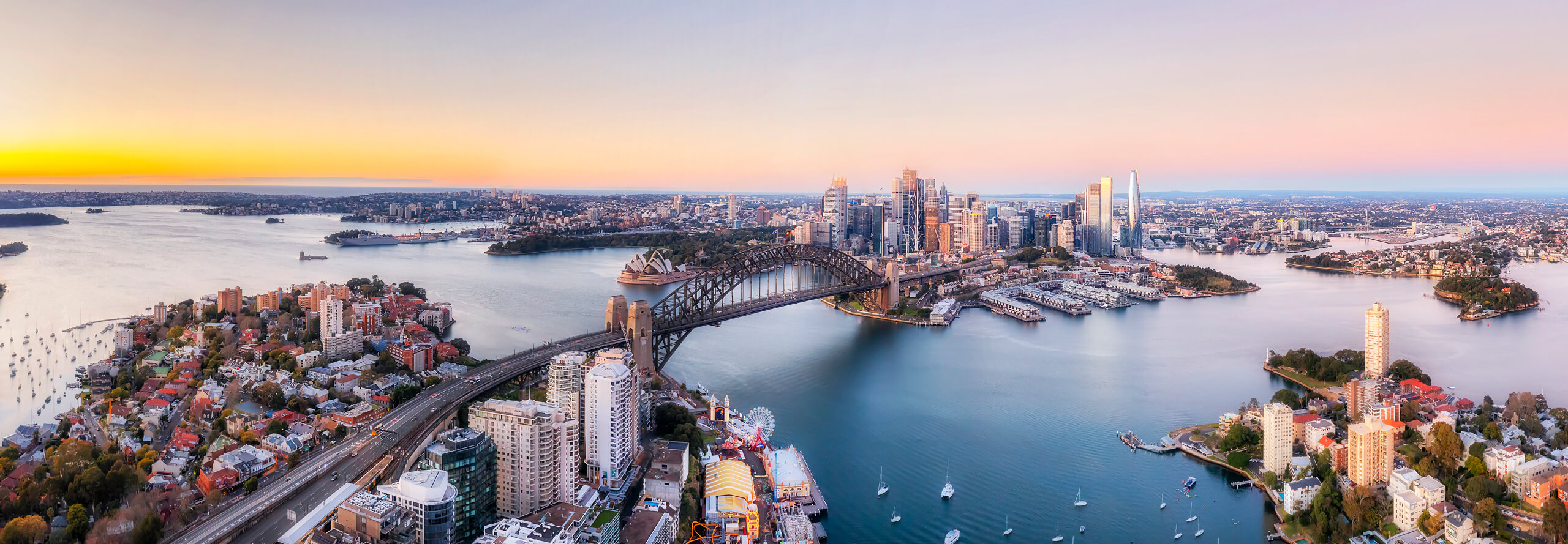 Aerial view of Sydney city at sunset, showcasing the skyline and vibrant colors reflecting on the water