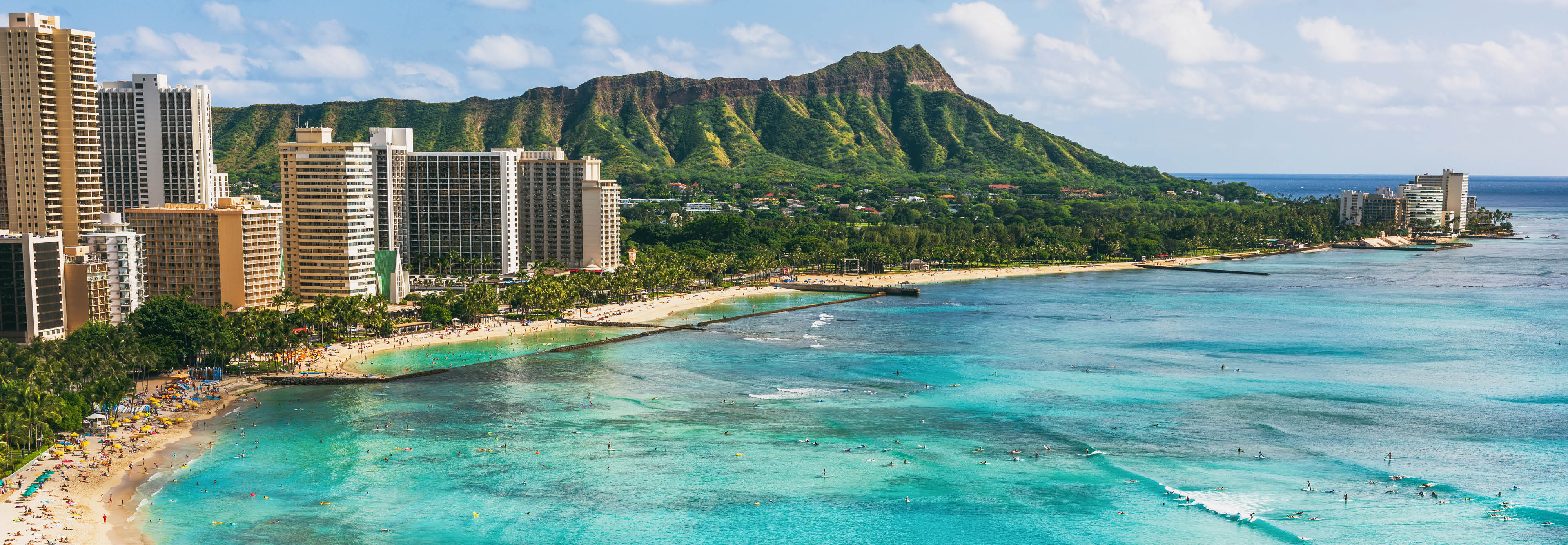 Stunning beach scene in Hawaii, showcasing soft sand, clear blue ocean, luxury hotels, and a backdrop of lush mountains