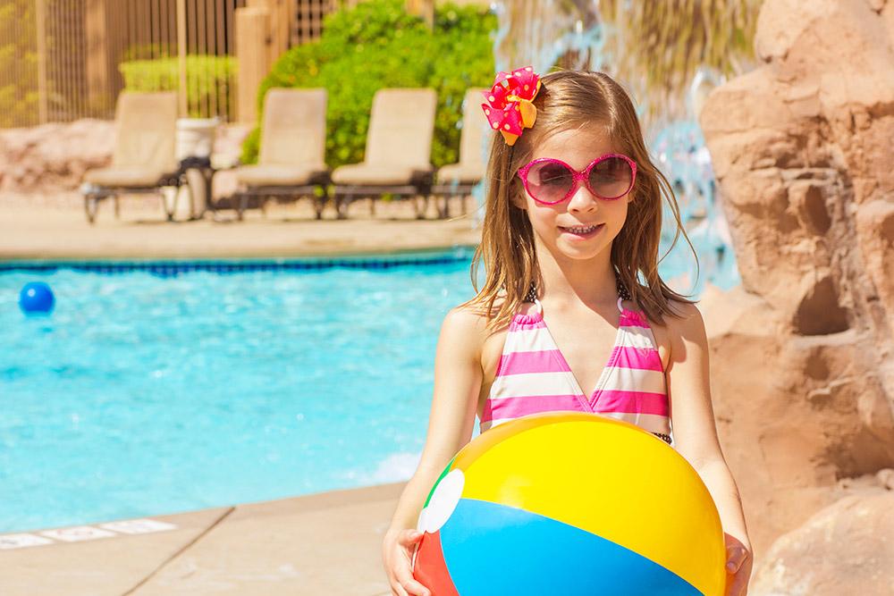 Child by a pool holding a beach ball