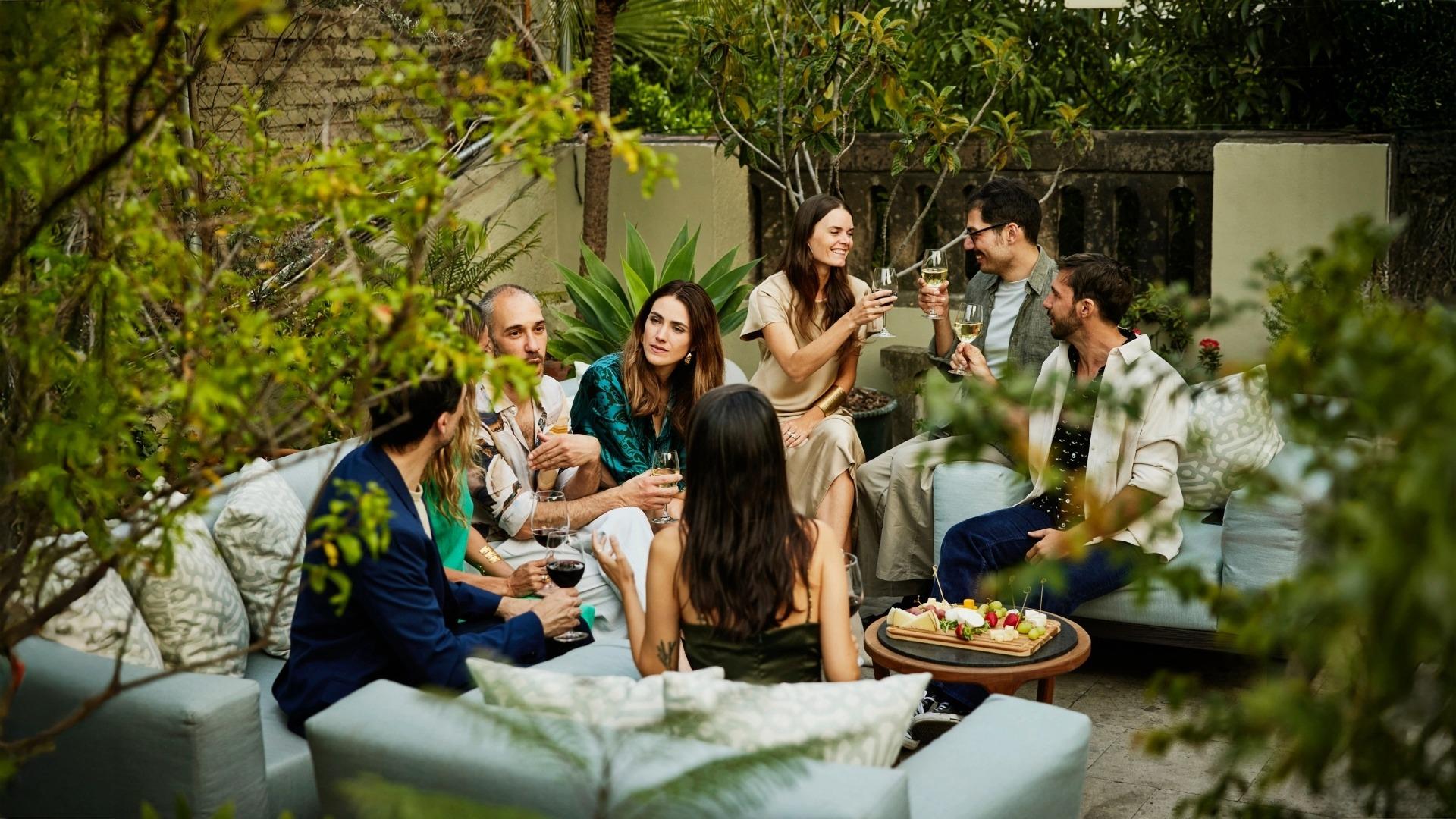 People sitting outside on couches sharing drinks and conversation with food tray nearby
