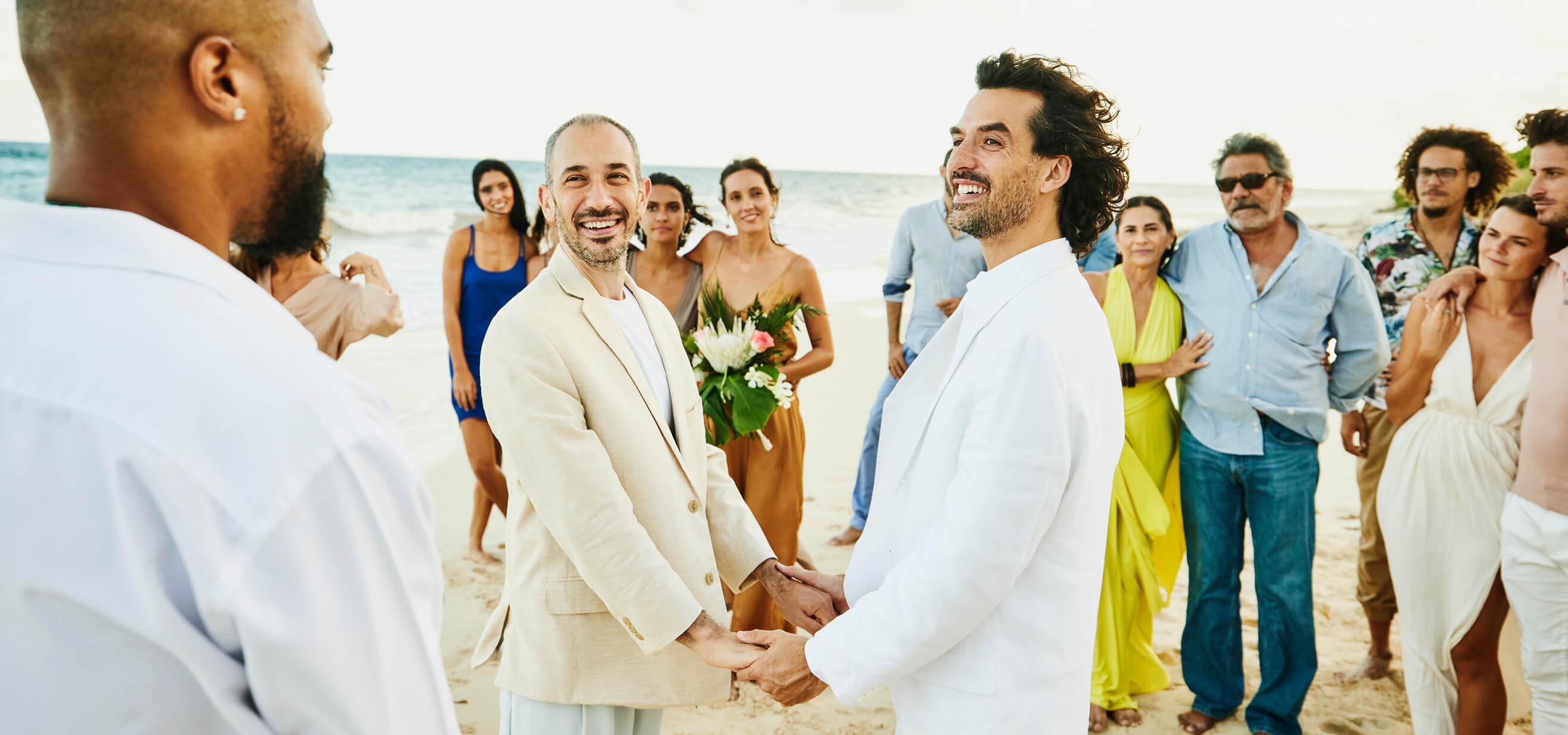 A pair of grooms and their wedding guests celebrate on the beach