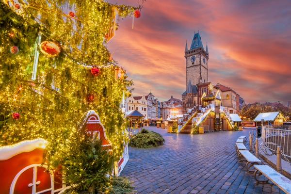 Christmas market with decorated tree and historic clock tower at sunset in Europe