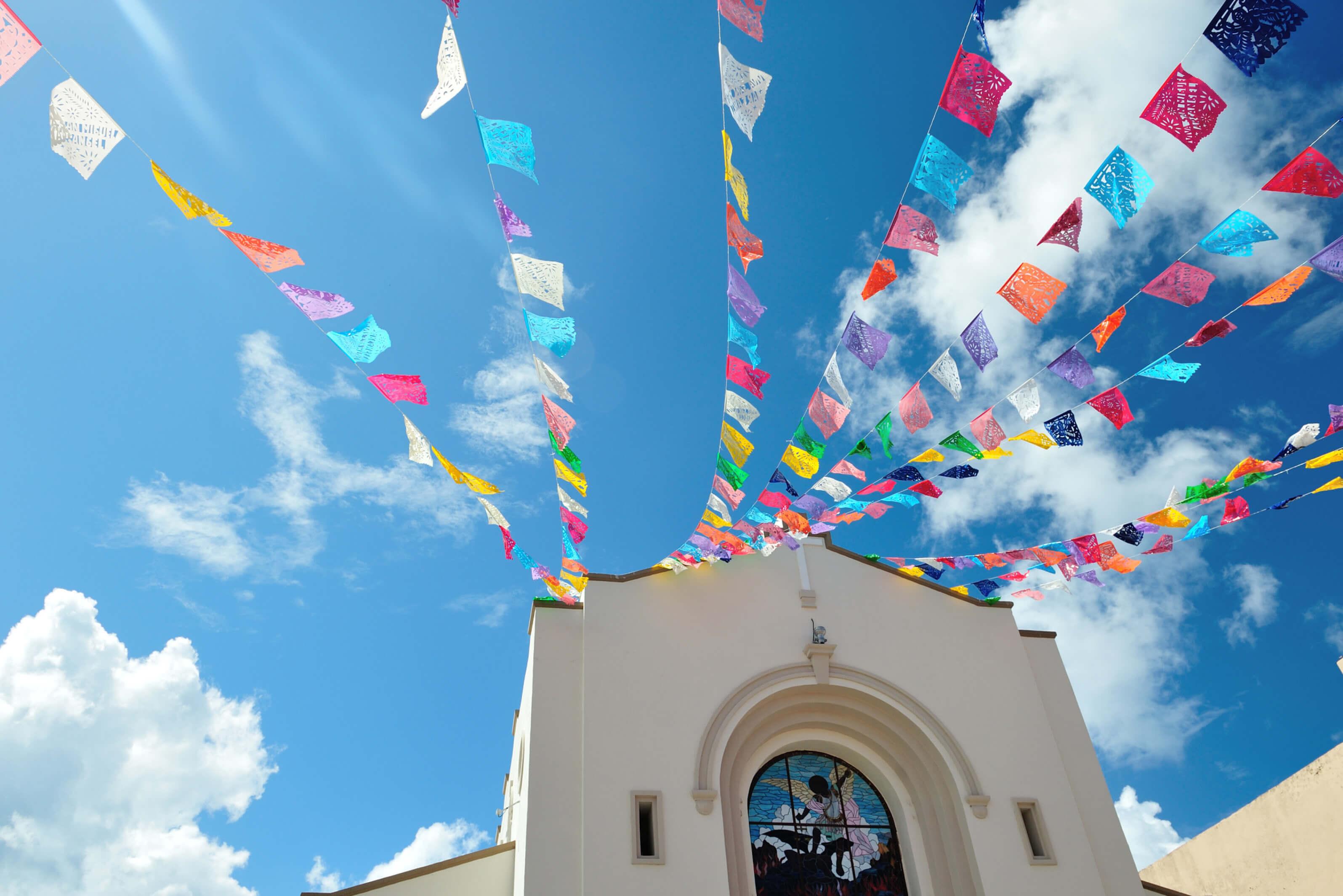 A church building in Cozumel, Mexico with a vibrant flags waving above its roof against a clear sky
