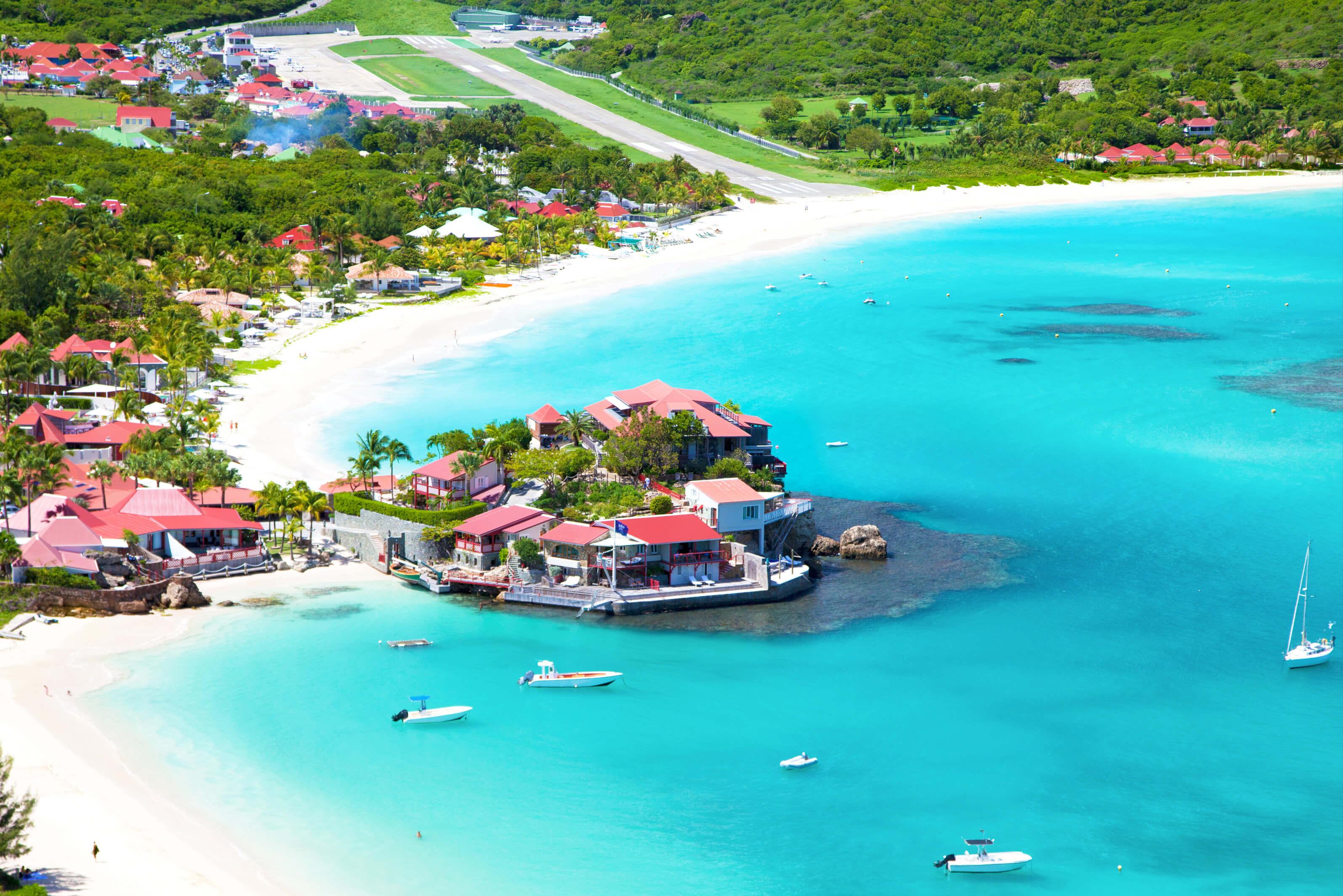 A vibrant beach scene with several boats and charming houses lining the coast of St. Barths