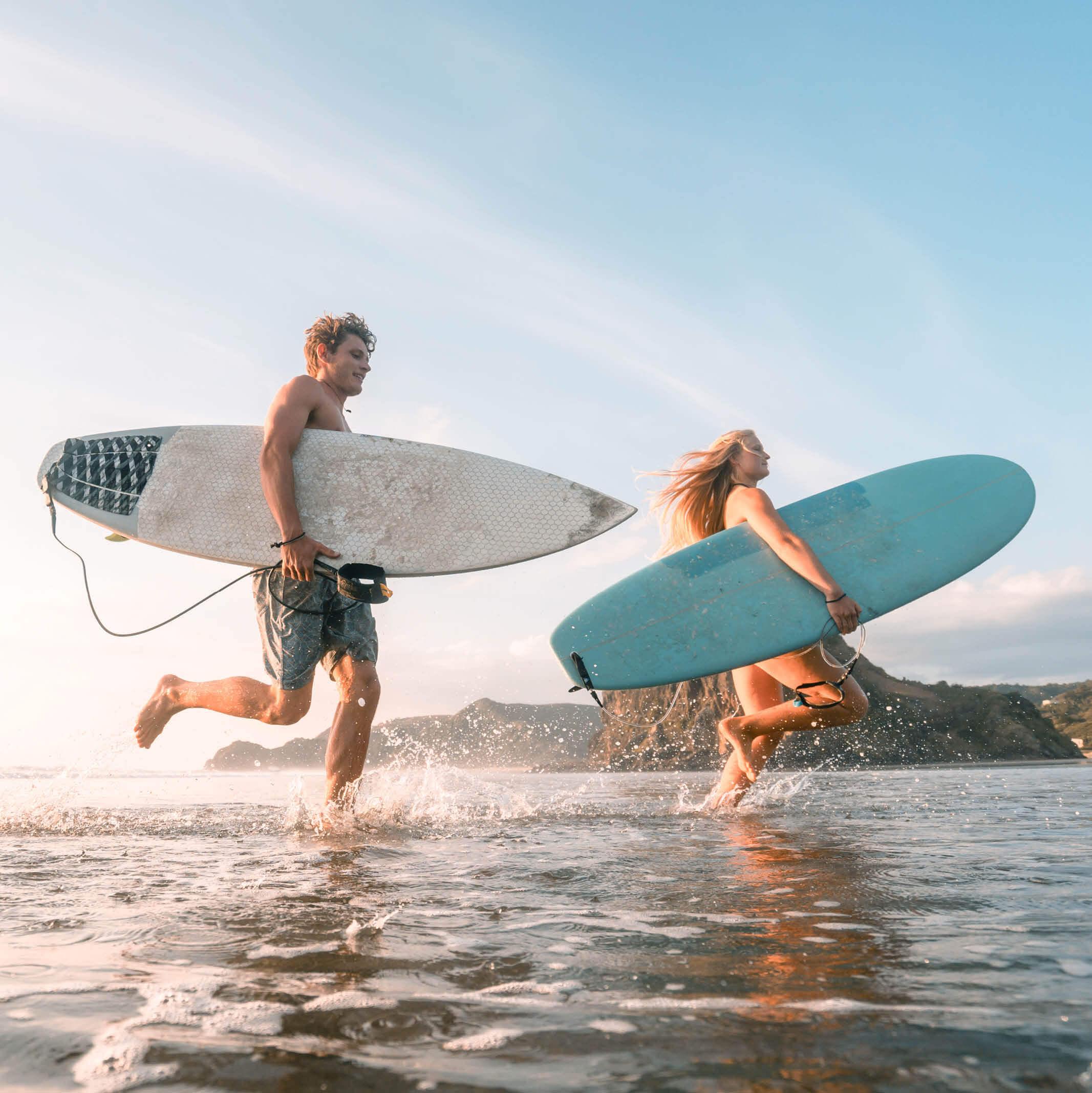 Two surfers run into the ocean holding their surfboards