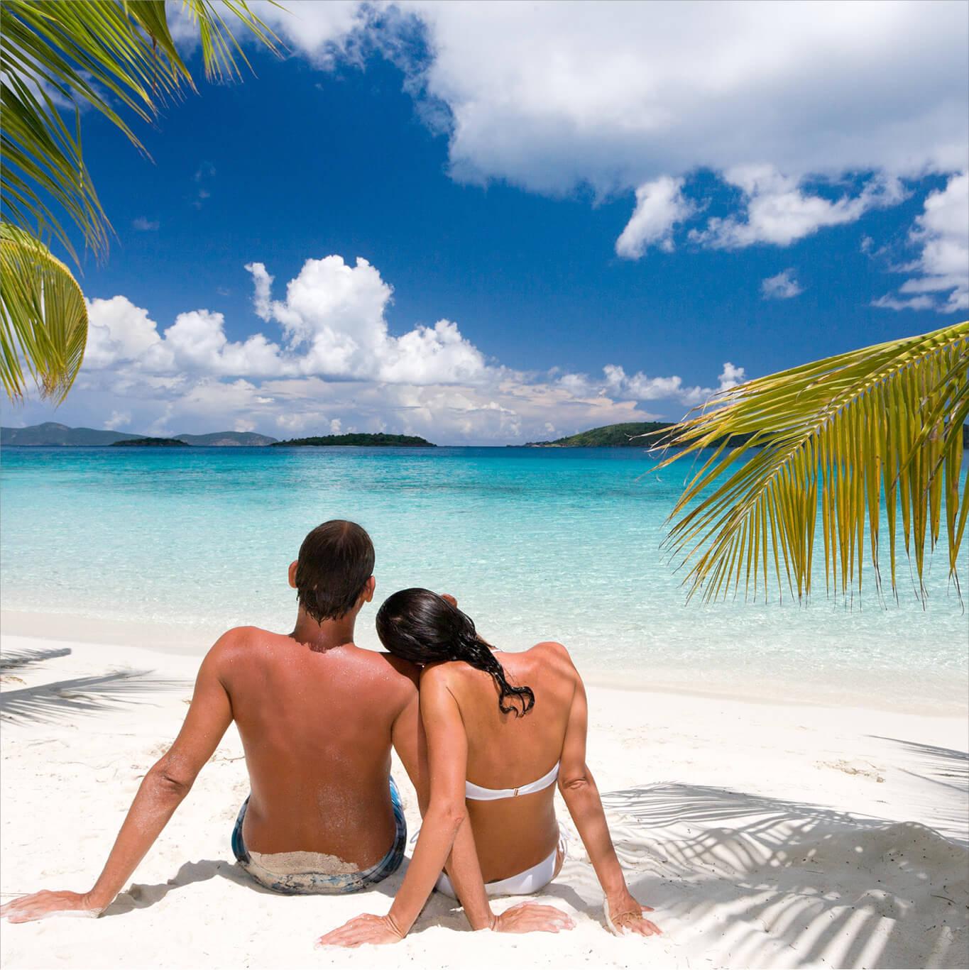 A couple lounges on the sand while looking out the ocean