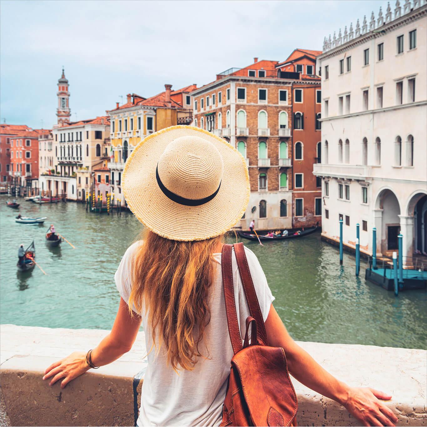 A woman is a sun hat overlooks a waterway in Venice, Italy