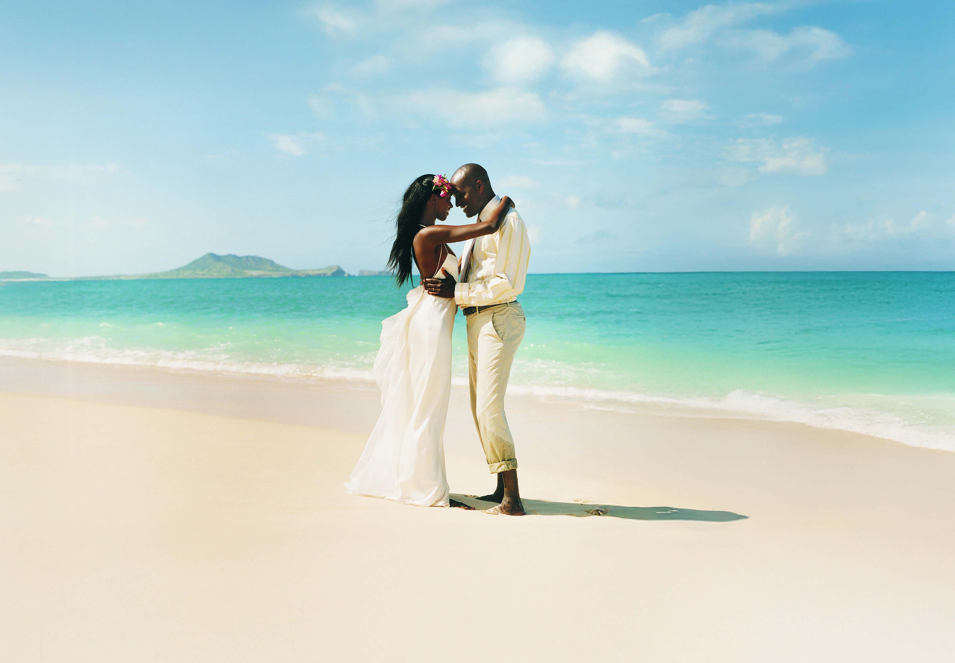 A newlywed couple in a wedding dress and suit embraces on a scenic beach